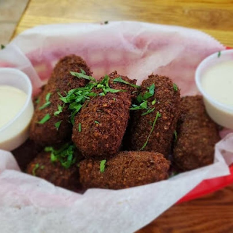 A basket of crispy, brown falafel pieces garnished with parsley, served with two dipping sauces.