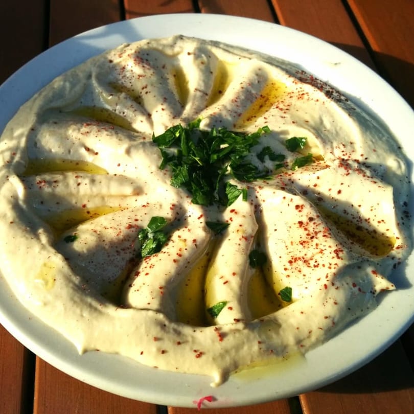 Creamy hummus drizzled with olive oil, sprinkled with paprika and fresh parsley on a white plate.