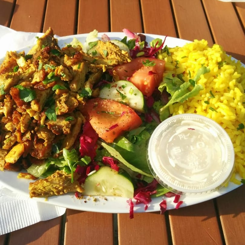 A halal Hut Plate with chicken, yellow rice, salad, and a side of white sauce.