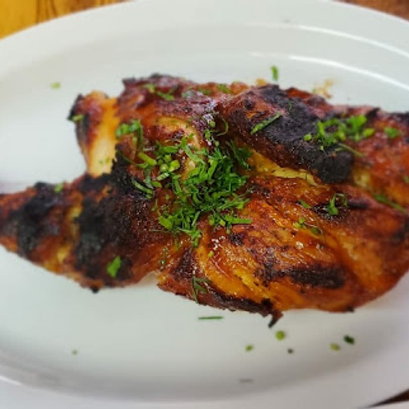 Halal grilled chicken, charred and golden brown, garnished with fresh green herbs on a white plate.
